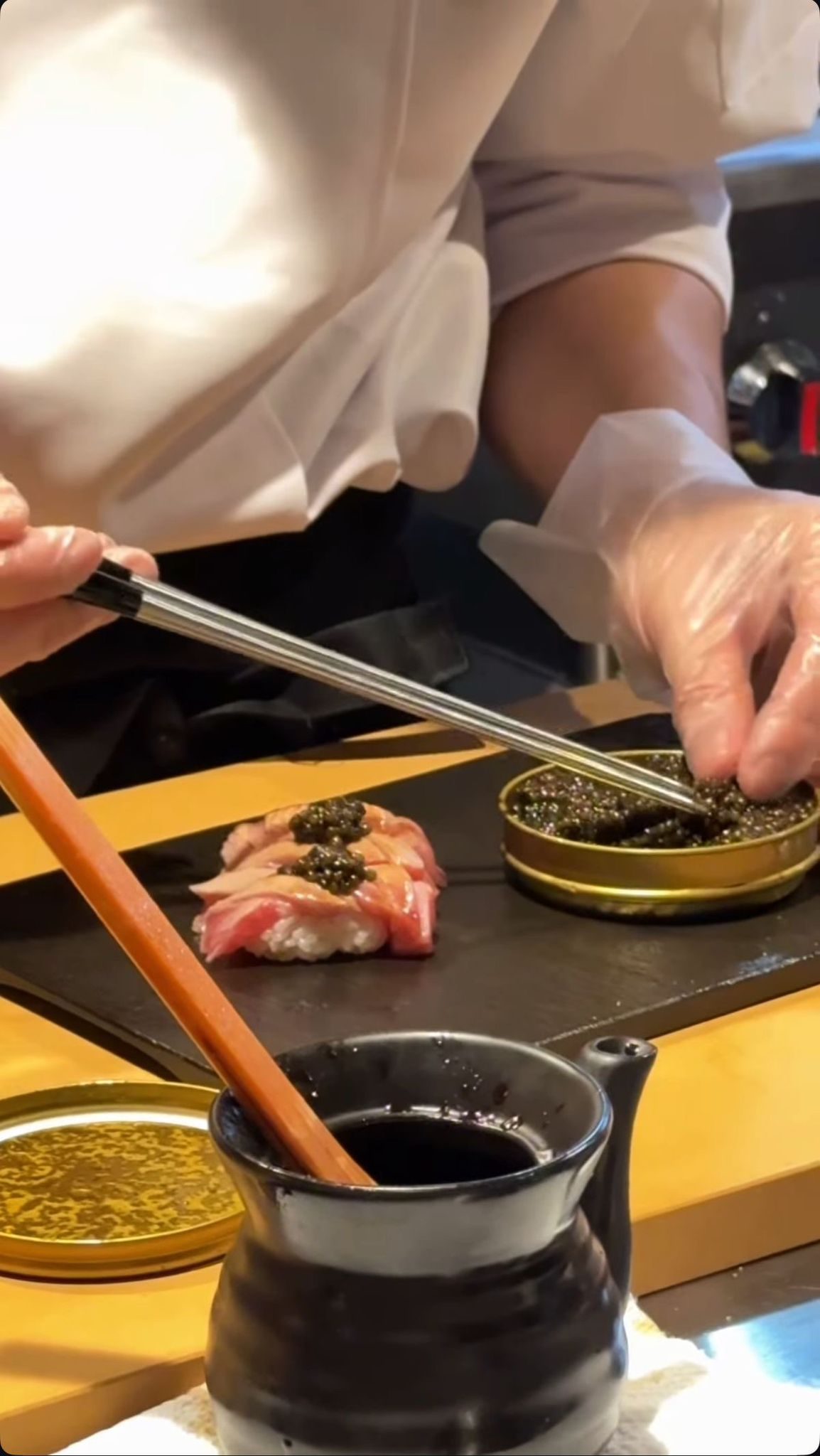 Hands finishing a bite with caviar, using chopsticks